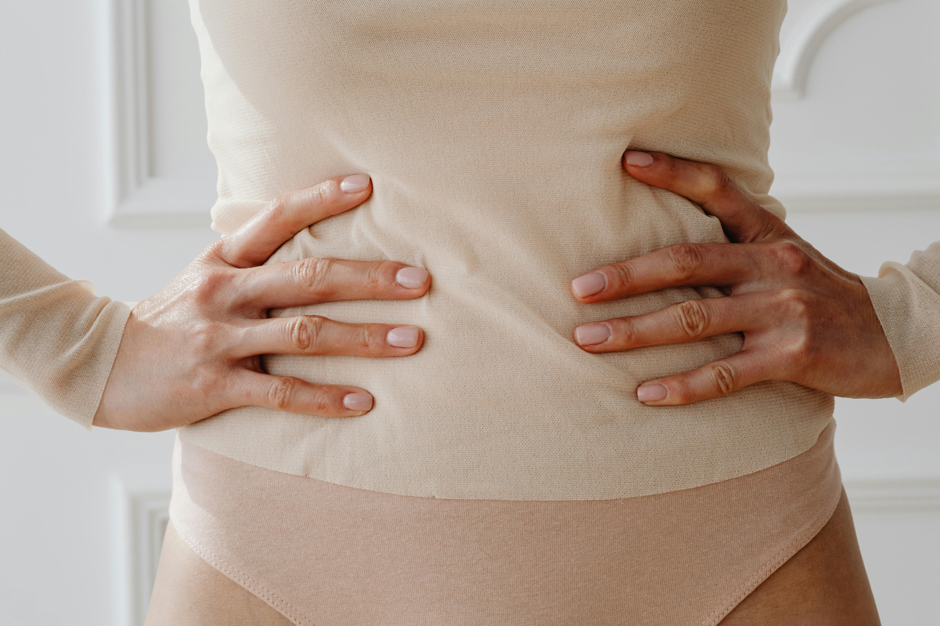 Femme avec les mains sur le ventre en vêtements beiges — le bouillon d'os soutient la santé intestinale, la paroi intestinale et le microbiome
